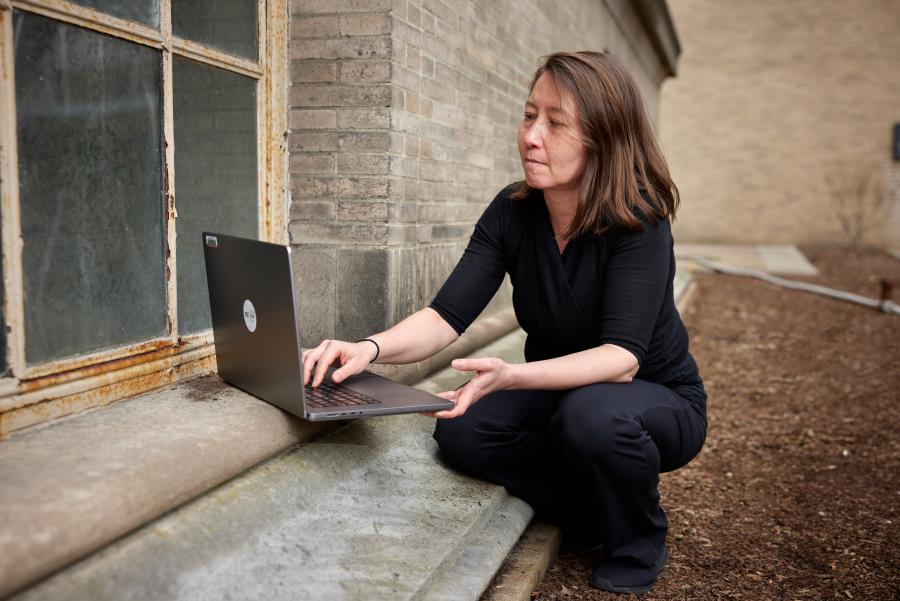 professor miho mazereeuw looks at a laptop near the base of building