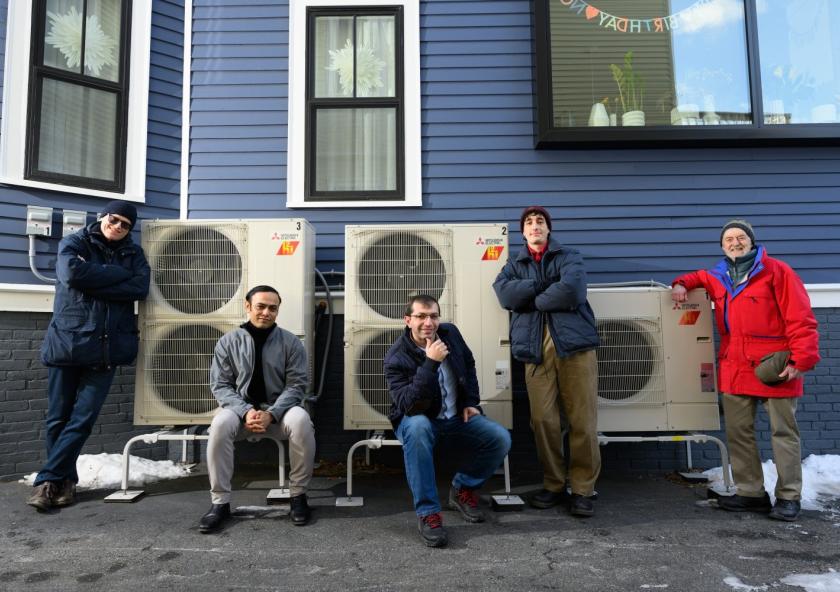 A modeling study by an MIT team has shown that electrifying residential heating can be a substantial step toward reducing carbon emissions, as well as costs, over the combined electricity and natural gas sectors. Here, the team poses beside a high-efficiency electric heat pump system that provides heating to the home, replacing the natural gas-fired furnace. Left to right: Audun Botterud, Saurabh Amin, Rahman Khorramfar, Morgan Santoni-Colvin, and Leslie Norford. Not pictured: Dharik Mallapragada.