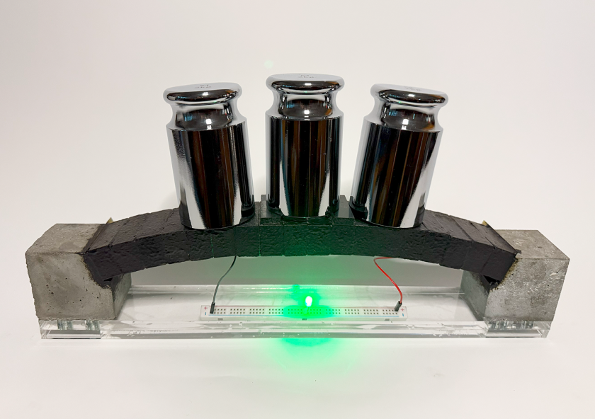 An electron-conducting carbon concrete (ec³)-based arch structure integrates supercapacitor electrodes for dual functionality. The prototype demonstrates both structural load bearing and the ability to power an LED, with the light’s intensity varying under applied load, highlighting the potential for real-time structural health monitoring via the supercapacitor. An electron-conducting carbon concrete (ec³)-based arch structure integrates supercapacitor electrodes for dual functionality. The prototype demonstrates both structural load bearing and the ability to power an LED, with the light’s intensity varying under applied load, highlighting the potential for real-time structural health monitoring via the supercapacitor.