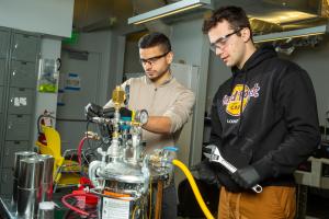 MIT engineers Aly Kombargi (left) and Niko Tsakiris (right) work on a new hydrogen reactor, designed to produce hydrogen gas by mixing aluminum pellets with seawater.