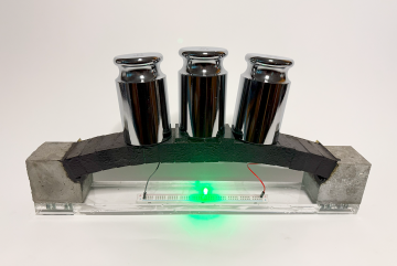 An electron-conducting carbon concrete (ec³)-based arch structure integrates supercapacitor electrodes for dual functionality. The prototype demonstrates both structural load bearing and the ability to power an LED, with the light’s intensity varying under applied load, highlighting the potential for real-time structural health monitoring via the supercapacitor.
