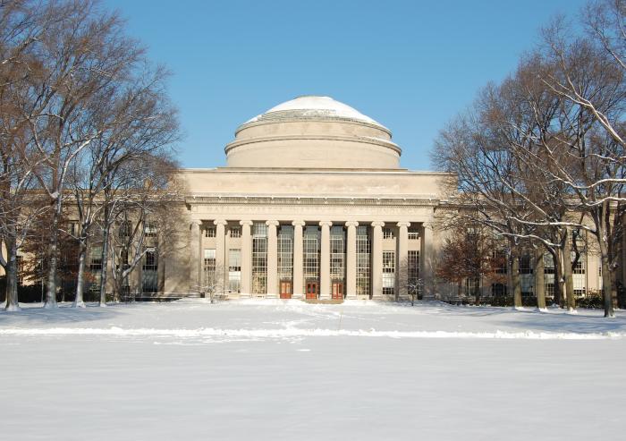 Snowy campus building with a large dome and tall columns framed by bare trees under a clear blue sky, conveying a serene winter scene.