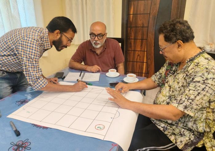 Left to right: Researchers Anamitra Saha and Sai Ravela of the MIT Department of Earth, Atmospheric and Planetary Sciences, and Jayanta Basu of the University of Calcutta design the board for a "snakes and ladders" game. The game is the first step in encouraging community members to use an app-based simulation that suggests solutions to their unique geographical and environmental challenges. 