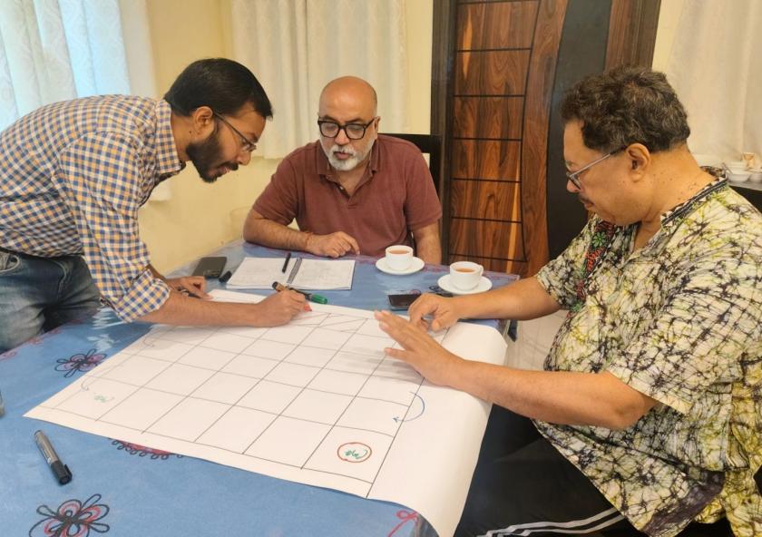 Left to right: Researchers Anamitra Saha and Sai Ravela of the MIT Department of Earth, Atmospheric and Planetary Sciences, and Jayanta Basu of the University of Calcutta design the board for a "snakes and ladders" game. The game is the first step in encouraging community members to use an app-based simulation that suggests solutions to their unique geographical and environmental challenges. 