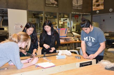 four students stand working at a table