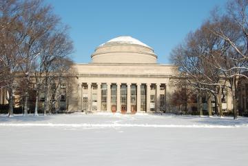 Snowy campus building with a large dome and tall columns framed by bare trees under a clear blue sky, conveying a serene winter scene.
