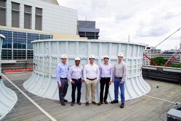On the roof of the Central Utility Plant building, standing in front of one of the cooling towers, are (left to right): Seth Kinderman, Central Utility Plant engineering manager; Kripa Varanasi, associate professor of mechanical engineering; recen...