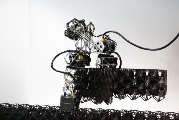 A robot carries three voxels as it walks across a voxel structure. Modular Inchworm Lattice Assembler robots, or MILAbots, use grippers on each end to place voxel building blocks and engage the snap-fit connections.