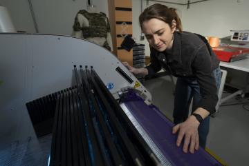 
              At Lincoln Laboratory’s Defense Fabric Discovery Center, Erin Doran demonstrates how reflective fibers can be woven into textiles. Such fibers could function as indelible, scannable labels to easily sort fabrics for recycling. 
   ...