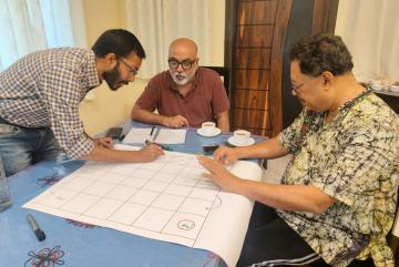 Left to right: Researchers Anamitra Saha and Sai Ravela of the MIT Department of Earth, Atmospheric and Planetary Sciences, and Jayanta Basu of the University of Calcutta design the board for a "snakes and ladders" game. The game is the first step in encouraging community members to use an app-based simulation that suggests solutions to their unique geographical and environmental challenges. 